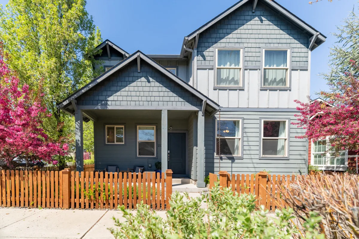 A lively front porch with colorful flower bushes, a wooden fence, and the textured siding of the home. The porch is a social space, ideal for relaxing outdoors or socializing with neighbors, with vibrant, welcoming curb appeal.