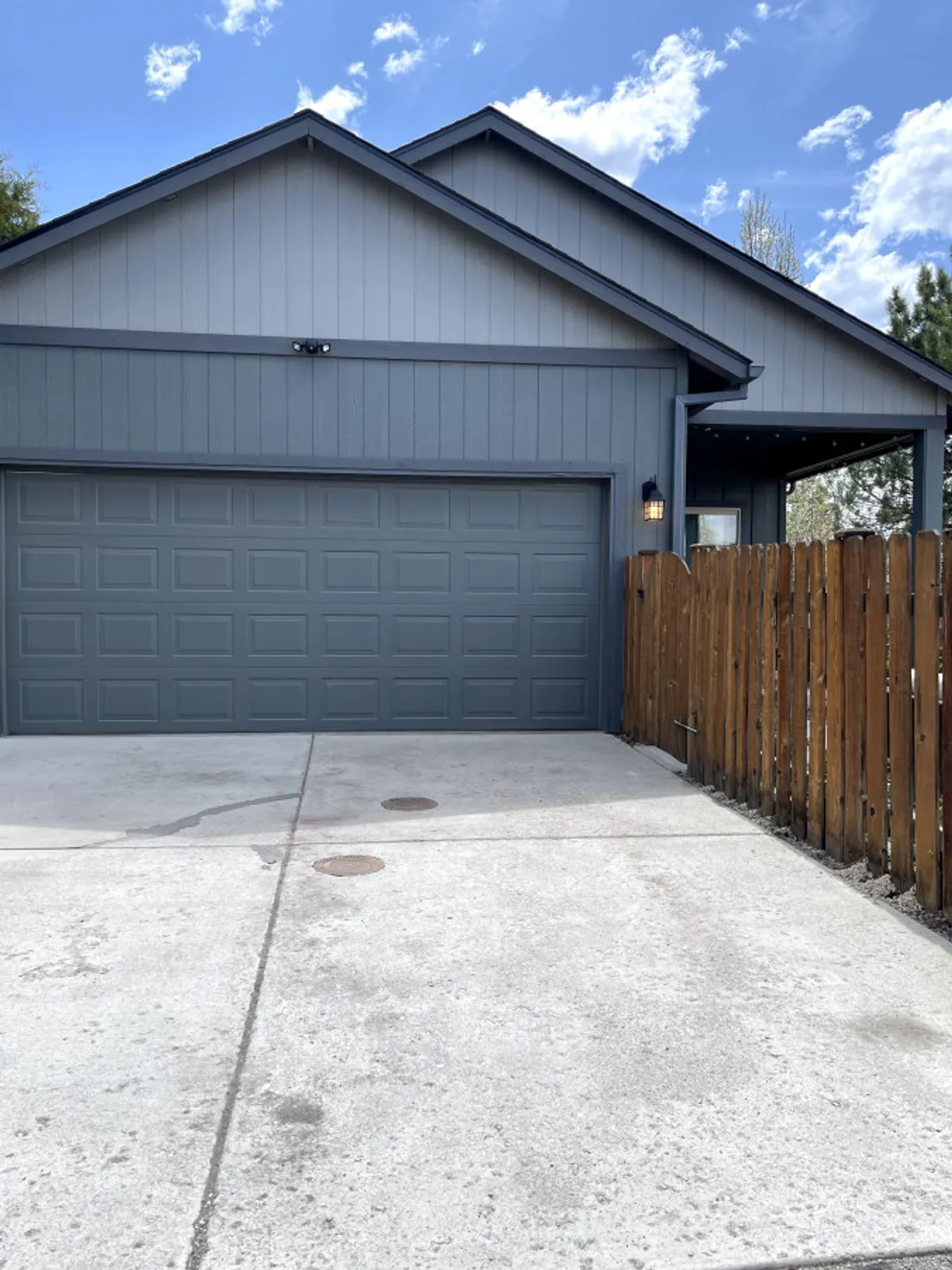 This exterior shot features the garage door and house facade, bordered by a wooden fence and illuminated by a welcoming light fixture. The scene conveys a sense of arrival and the practical convenience of daily living in a friendly neighborhood.