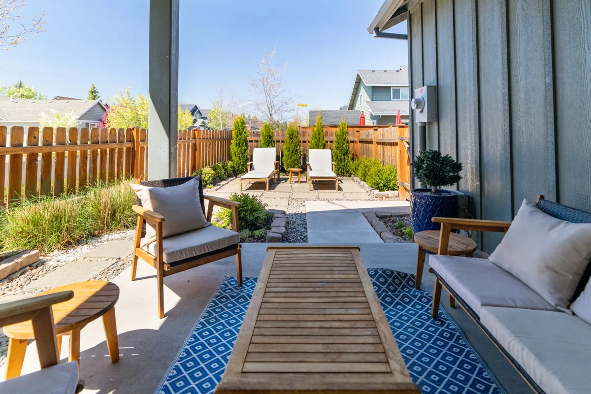 A serene patio setup with outdoor lounge chairs, a wooden coffee table, and lush greenery, perfect for enjoying the fresh air. The area is inviting for relaxation, reading, or socializing, and hints at views beyond the immediate garden.