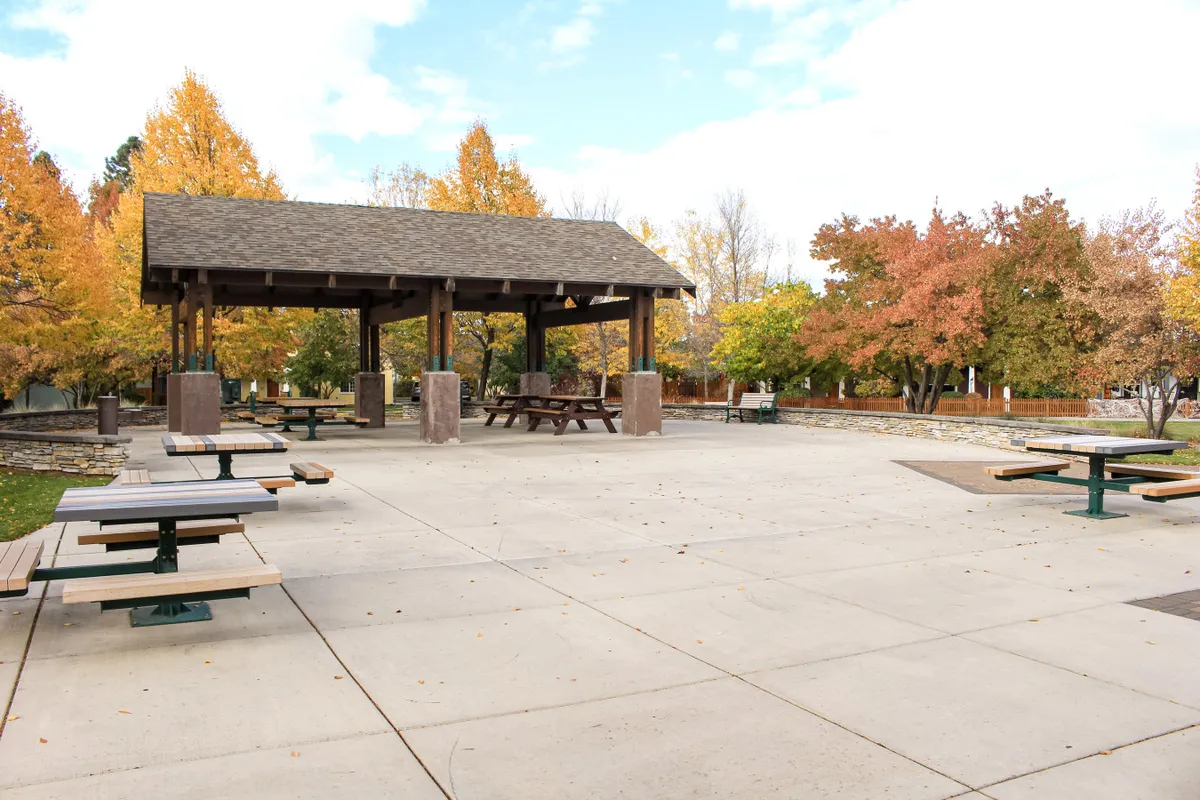 A community pavilion surrounded by picnic tables and mature trees, inviting guests to picnic, gather for sunset viewings, or participate in local events. The ambiance promotes relaxation and neighborly interaction.