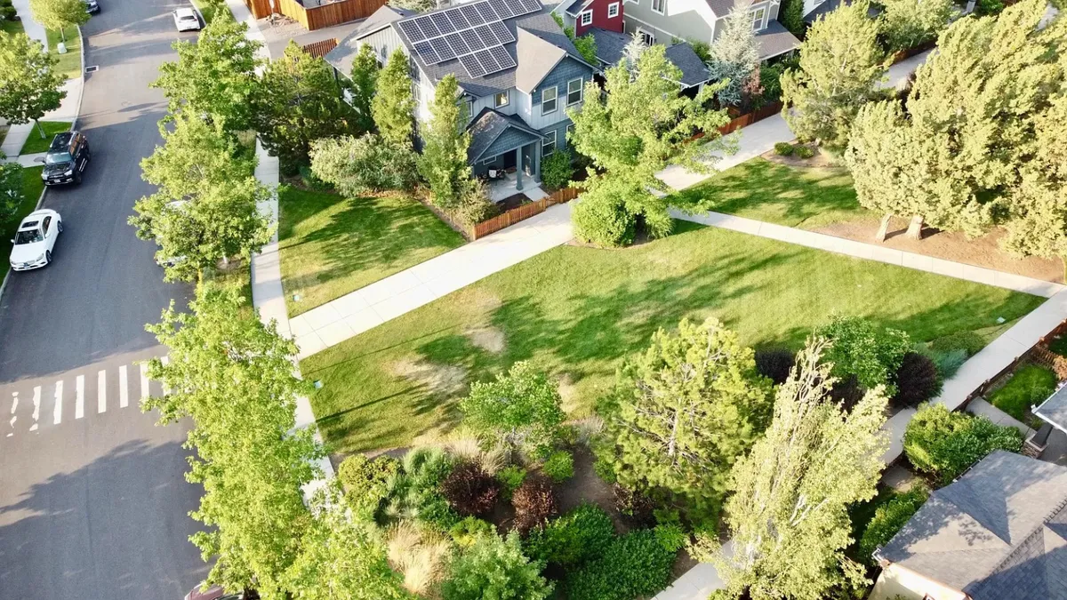 A tranquil neighborhood park scene featuring manicured lawns, tree-lined paths, and residential homes in the background. The setting is ideal for quiet strolls, light exercise, or peaceful moments under the trees.